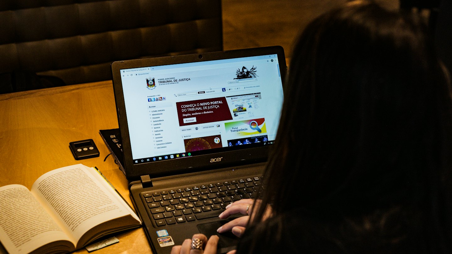 Person working on a laptop with an open book on a table.